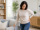 Woman holding her outer hip while supporting herself on a sofa