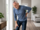 Older man holding his lower back while experiencing back and leg discomfort