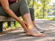 Person holding a painful ankle while seated on an outdoor bench